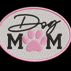 May include: Embroidered oval patch with the words "Dog Mom" in black script and block letters. A pink paw print is centered between the letters "M". The patch has a pink border and a light gray background.