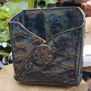 Pu&ograve; includere: Un vaso quadrato in ceramica con smalto blu scuro e verde. Il vaso presenta un motivo strutturato e un bottone decorativo con un motivo floreale. Il vaso &egrave; alto circa 15 cm e largo 13 cm.
