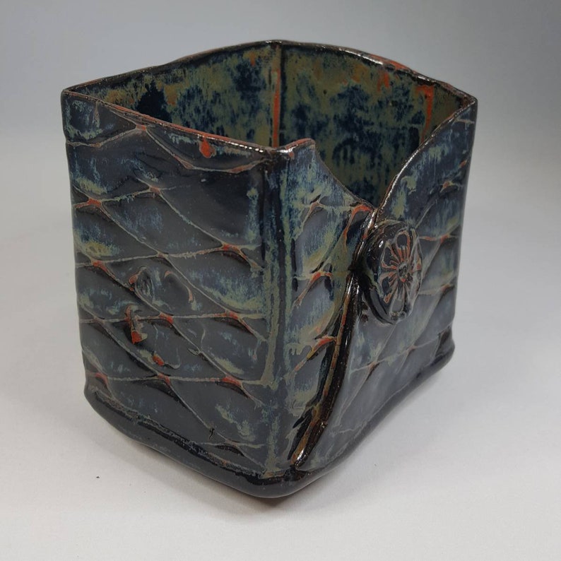 Pu&ograve; includere: Contenitore in ceramica fatto a mano con motivo trapuntato. L'esterno blu scuro ha accenti verdi e arancioni. Un bottone decorativo &egrave; sul lato. Il contenitore di forma quadrata &egrave; adatto per contenere piccoli oggetti.