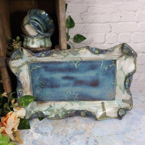 May include: Handmade ceramic serving tray with a rectangular shape and a wavy, decorative edge. The tray features a blue and white glaze with a textured surface. Two matching ceramic bowls are stacked in the background. The pottery has a rustic, artisanal aesthetic.