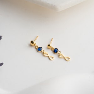 May include: A pair of gold earrings with a blue gemstone and an infinity symbol.