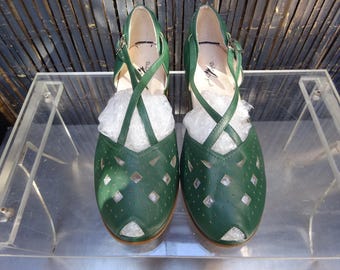 May include: A pair of forest green leather shoes featuring a peep-toe design, a cutout diamond pattern across the vamp, and thin crisscross ankle straps with metal buckles. The interior insoles are light-colored and feature a black logo print.