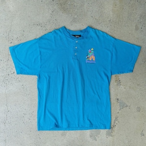 Könnte beinhalten: Ein türkisfarbenes Kurzarm-Shirt mit Henley-Ausschnitt. Das Shirt zeigt eine farbenfrohe Grafik eines Schlosses, Mickey Mouse und den Text "Disneyland" auf der Vorderseite. Das Shirt ist aus weichem Material.