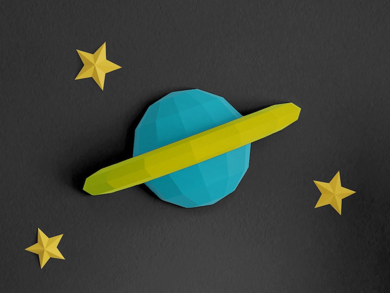 Pu&ograve; includere: Un'opera di carta di un pianeta blu e giallo con anelli su uno sfondo nero. Ci sono tre stelle di carta gialle sparse intorno al pianeta.