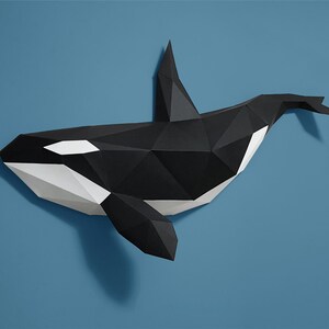 May include: An origami orca whale sculpture, made from paper and featuring a geometric design. The sculpture is black and white.