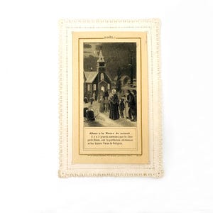 Pode incluir: Um cartão retangular de cor creme com uma borda recortada apresentando uma impressão bege centralizada. A imagem mostra uma cena noturna nevada com uma igreja, pessoas e o texto NOËL, Allons à la Messe de minuit, Il y a 3 grands.