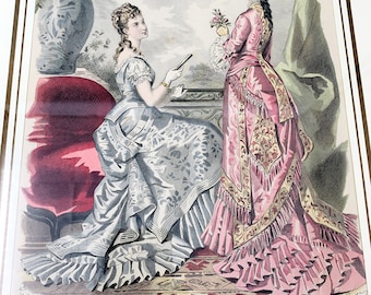 May include: Two women in elaborate dresses pose for a fashion illustration. The woman on the left wears a light blue dress with a floral pattern. The woman on the right wears a pink dress with gold embroidery and a long train. The illustration is framed and has the text "L'Europe a Paris" at the bottom.