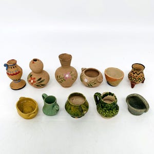Op de afbeelding: Een verzameling van tien kleine, handbeschilderde terracotta potten in verschillende vormen en maten. De potten zijn versierd met bloem- en geometrische patronen in tinten bruin, groen, geel en wit.