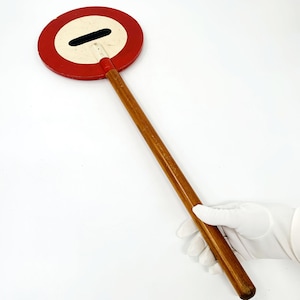 Puede incluir: Una señal de tráfico circular roja y blanca con una barra horizontal negra en el centro, montada en un palo de madera largo.