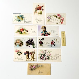 Könnte beinhalten: Eine Sammlung antiker Postkarten mit Blumenarrangements, Porträts und handschriftlichem Text. Die Karten zeigen verschiedene Farben, darunter Rot, Rosa, Blau und Grün, mit französischen Sätzen wie "Bonne Année" und "Vive Ste Catherine."