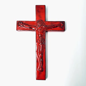 Op de afbeelding: Een rode kruisbeeld met een gedetailleerde afbeelding van Jezus Christus. Het kruis is dieprood van kleur met een glanzende afwerking en de figuur van Christus is ingewikkeld gesneden, wat het religieuze thema benadrukt.