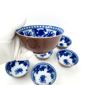 Op de afbeelding: Set van zes kleine blauwe en witte porseleinen kommen met een bruine glazuur. De kommen hebben een bloemmotief en een gegolfde rand.