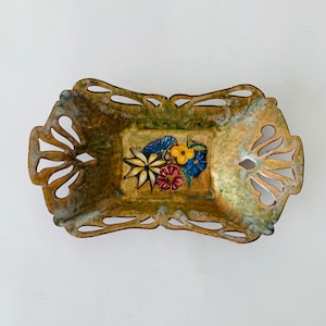 Op de afbeelding: Een decoratieve metalen schaal met een uitgesneden ontwerp en een geschilderd bloemenmotief in tinten geel, rood, blauw en groen.