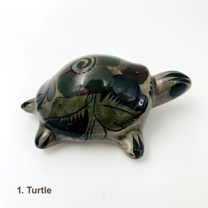 May include: Hand-painted ceramic turtle figurine with black, green and red floral designs. The turtle is in a walking position with its head turned to the side.