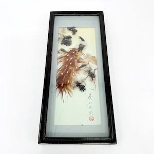 May include: A framed artwork featuring a peacock made of feathers, with a black frame and a white background. The artwork includes Japanese calligraphy and a red seal.