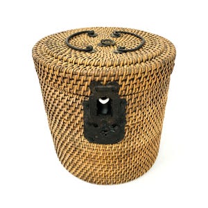 Può includere: Un cesto rotondo in vimini intrecciato con una chiusura in metallo e dettagli decorativi in metallo sul coperchio.