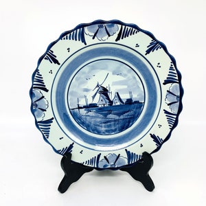 May include: A blue and white ceramic plate with a windmill scene. The plate has a scalloped edge and a floral design.