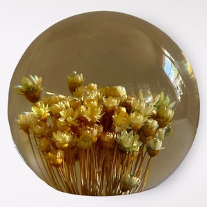 Puede incluir: Un pisapapeles de vidrio transparente con un grupo de flores amarillas secas en su interior. Las flores están dispuestas en forma de ramo y tienen una estética delicada y vintage.