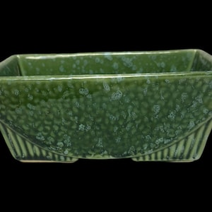 May include: A green ceramic planter with a textured surface and a rectangular shape. The planter has a slightly flared lip and a rounded bottom.