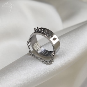 May include: A silver ring with a chain attached. The ring has a row of spikes on the top and the words "DARK & WILD" engraved on the inside.