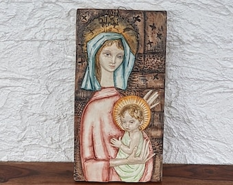 May include: A ceramic wall plaque depicting the Virgin Mary holding baby Jesus. The plaque is brown with a textured surface and features a halo around the head of each figure. The Virgin Mary is wearing a blue robe and a crown. Baby Jesus is wearing a green robe.