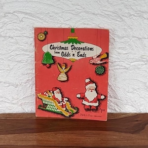 May include: A vintage red booklet titled "Christmas Decorations from Odds 'n' Ends" with illustrations of Santa Claus, a Christmas tree, and other festive decorations. The booklet is a Pack-o-Fun publication.