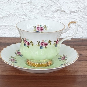 Puede incluir: Un juego de taza y platillo de té verde y blanco con un patrón floral. La taza tiene un borde dorado y un asa. El platillo tiene un borde festoneado.
