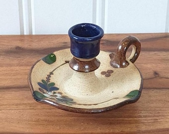 Könnte beinhalten: Ein Kerzenhalter aus Keramik mit einer dunkelblauen Tasse, einem braunen Sockel und einer beigefarbenen Platte mit floralen Mustern. Der Halter hat einen kleinen Griff und steht auf einer Holzoberfläche. Der Kerzenhalter ist ein dekorativer Artikel.
