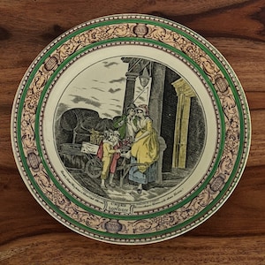Puede incluir: Un plato de cerámica vintage con un borde verde y dorado. El centro presenta una ilustración en blanco y negro de personas en una escena callejera. El texto "CRIES OF LONDON" está impreso en el plato.