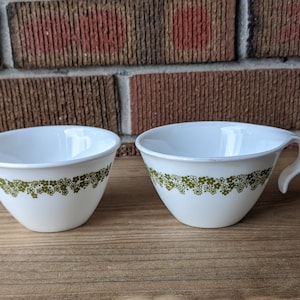 May include: Two white ceramic bowls with a green floral pattern. One bowl has a handle.