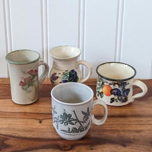 Peut inclure: Quatre tasses en céramique avec des motifs floraux et fruités. Les tasses sont toutes de couleurs et de motifs différents. Elles sont posées sur une surface en bois.