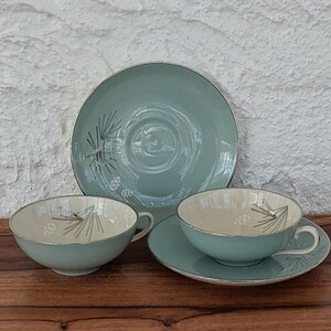 Peut inclure: Un ensemble de trois tasses à thé et soucoupes vintage avec un glaçage bleu clair et un motif de pin en argent. Les tasses et les soucoupes ont un intérieur blanc.
