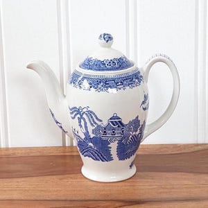 May include: A white ceramic teapot with a blue and white willow pattern. The teapot has a lid and a spout.
