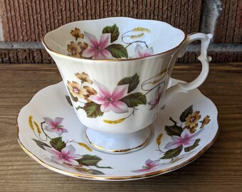 May include: A white teacup and saucer with a floral pattern. The cup has a delicate handle and a gold rim. The saucer has a matching floral pattern and a gold rim.
