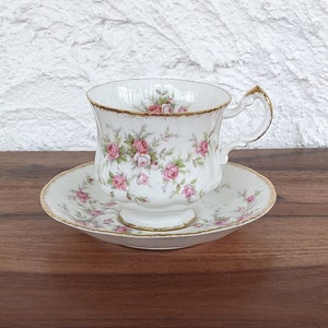 May include: A white teacup and saucer with a pink rose floral pattern and gold trim.