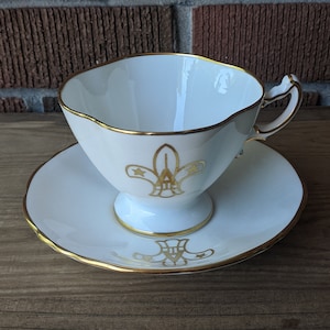 Xícara de chá e pires Hammersley & Co, flor de lis branca e dourada com a letra "A", Bone China, fabricada na Inglaterra, década de 1950