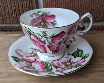 Puede incluir: Un juego de taza y platillo de té blanco con un diseño floral. La taza y el platillo presentan flores rosas y verdes con ribetes dorados.