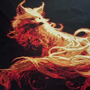 May include: A tapestry featuring a stylized, fiery fox design. The artwork uses a pixelated style with shades of red, orange, and cream against a black background. The fox's fur appears to be flowing, creating a dynamic visual.