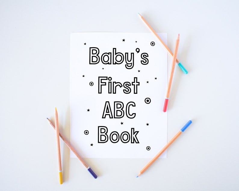 Pu&ograve; includere: Un foglio di carta bianco con il testo "Baby's First ABC Book" stampato in nero. Quattro matite colorate sono appoggiate sul foglio.