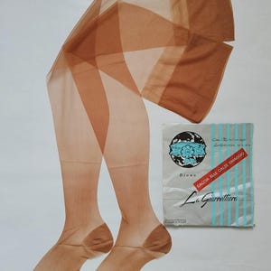May include: Sheer, tan-colored stockings with a geometric pattern, laid out on a white surface. The stockings are paired with a vintage package featuring the text "Diana" and "La Garrettiera". The package has blue stripes and Italian text.