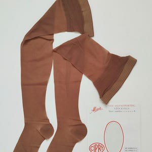 May include: A white ceramic mug with a black handle and the text "But First, Coffee" in a black, handwritten-style font. The mug is on a white surface.