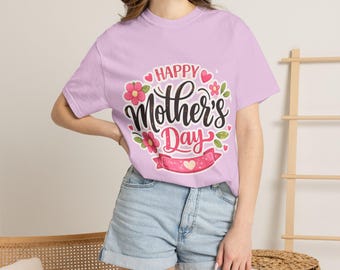 May include: A lilac t-shirt featuring the text "Happy Mother's Day" in a decorative script, encircled by pink flowers and a pink banner. The shirt is a short-sleeved crew neck.