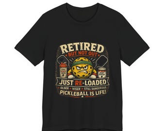 May include: Black t-shirt with a graphic featuring a pickleball character and the text "RETIRED BUT NOT OUT JUST RE-LOADED". The design includes pickleball paddles, water bottle, and joint support. The phrase "PICKLEBALL IS LIFE!" is also included.