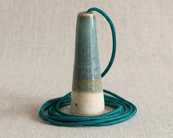 May include: A ceramic light pull with a tapered, conical shape featuring a gradient glaze that transitions from a speckled cream base to a muted green top, attached to a long, coiled teal nylon cord for ceiling switch operation.
