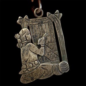 Könnte beinhalten: Silberfarbener Anhänger mit einem detaillierten Relief einer Figur, die vor einer Struktur kniet. Der Anhänger hat ein aufwendiges Design mit geometrischen Mustern und eine Schlaufe zum Aufhängen. Die Figur hält einen Gegenstand, und der Stil deutet auf ein antikes oder historisches Thema hin.