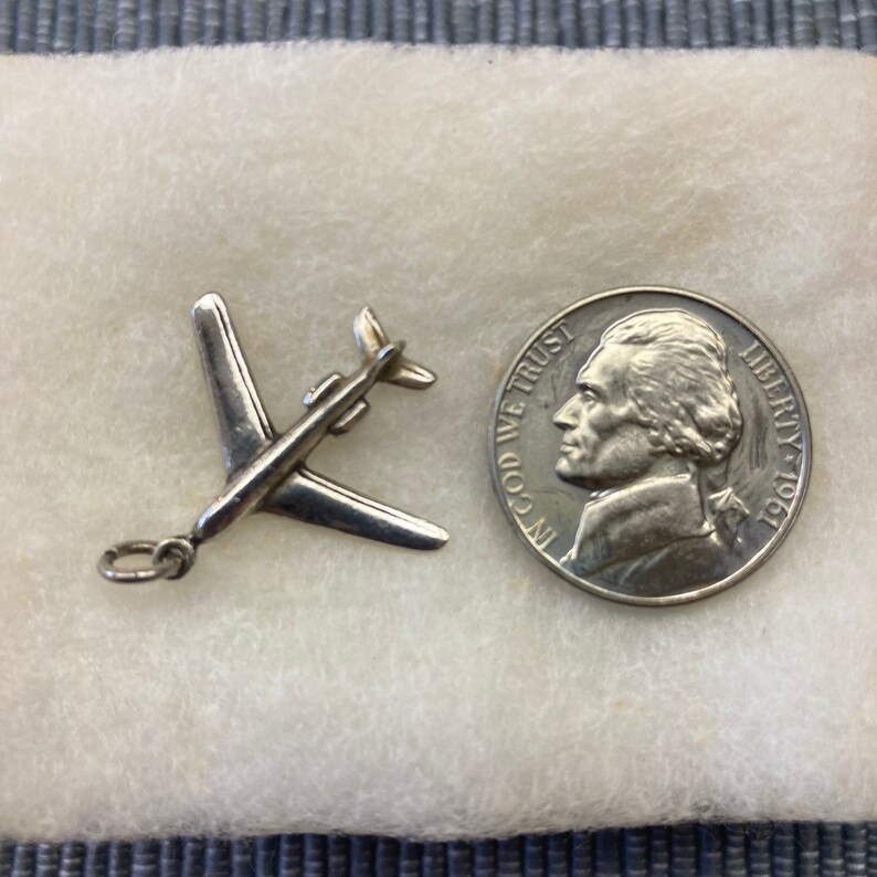 May include: A silver airplane charm, approximately the size of a US nickel, with a loop for attaching to a chain or bracelet.