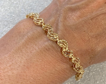 May include: A gold bracelet with a textured, wavy design. The bracelet is made of a delicate chain and has a polished finish.