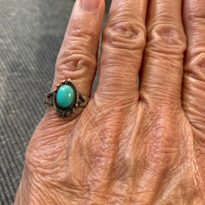 K&ouml;nnte beinhalten: Ein silberner Ring mit einem t&uuml;rkisfarbenen Stein, der in einer silbernen Fassung sitzt. Der Ring befindet sich an einem Finger.