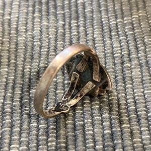 K&ouml;nnte beinhalten: Ein silberner Ring mit einem detaillierten Design, das einen dunkelblauen Stein zeigt.