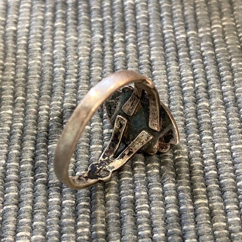 K&ouml;nnte beinhalten: Ein silberner Ring mit einem detaillierten Design, das einen dunkelblauen Stein zeigt.